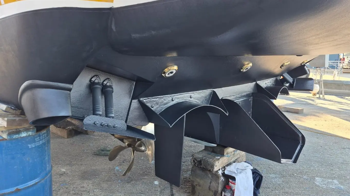 Close-up of a boat's hull showing the propeller, stabilisers, and water intake systems, positioned on a sturdy stand.
