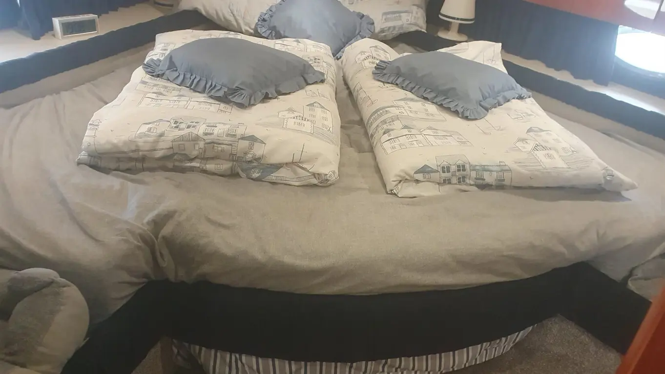 A spacious bed with grey bedding and patterned pillows is arranged in a stylish room, featuring a lamp and clock.