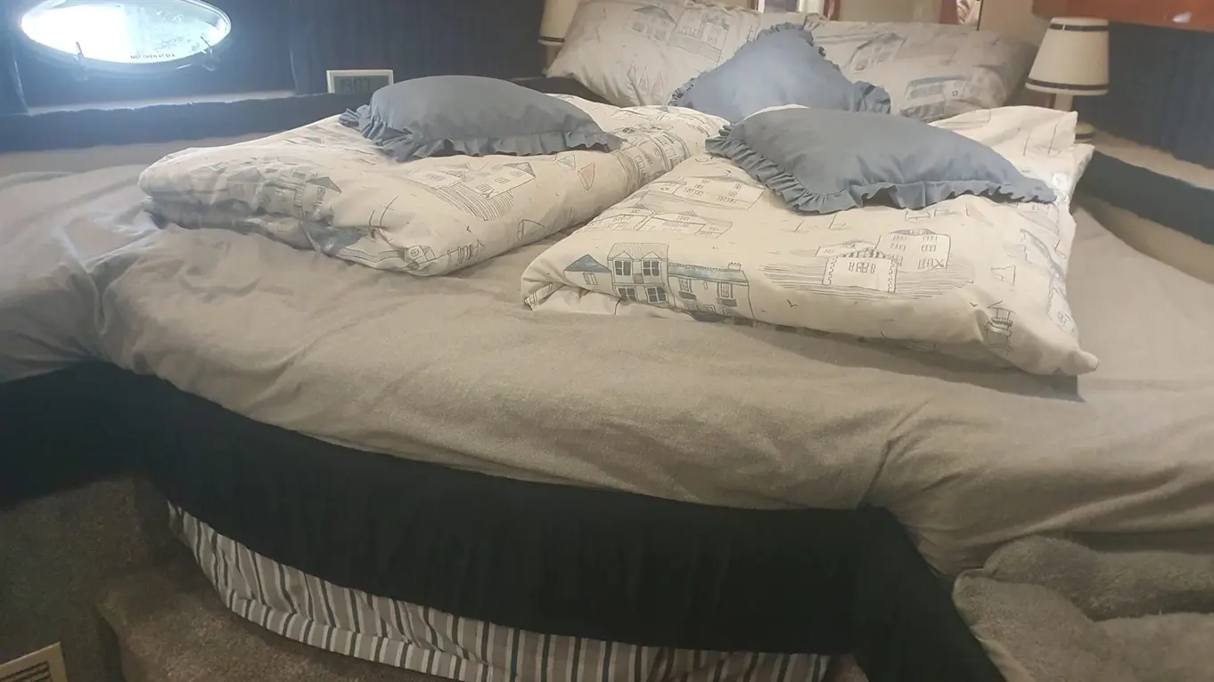Double bed with patterned cushions and blankets, featuring wooden paneling and a round window in a cosy cabin setting.