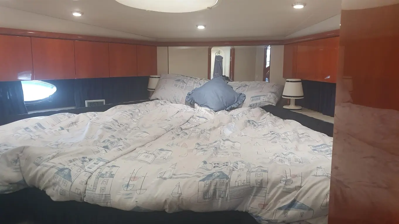 Luxurious boat bedroom featuring a large bed with nautical-themed bedding, wood cabinetry, and a porthole window.