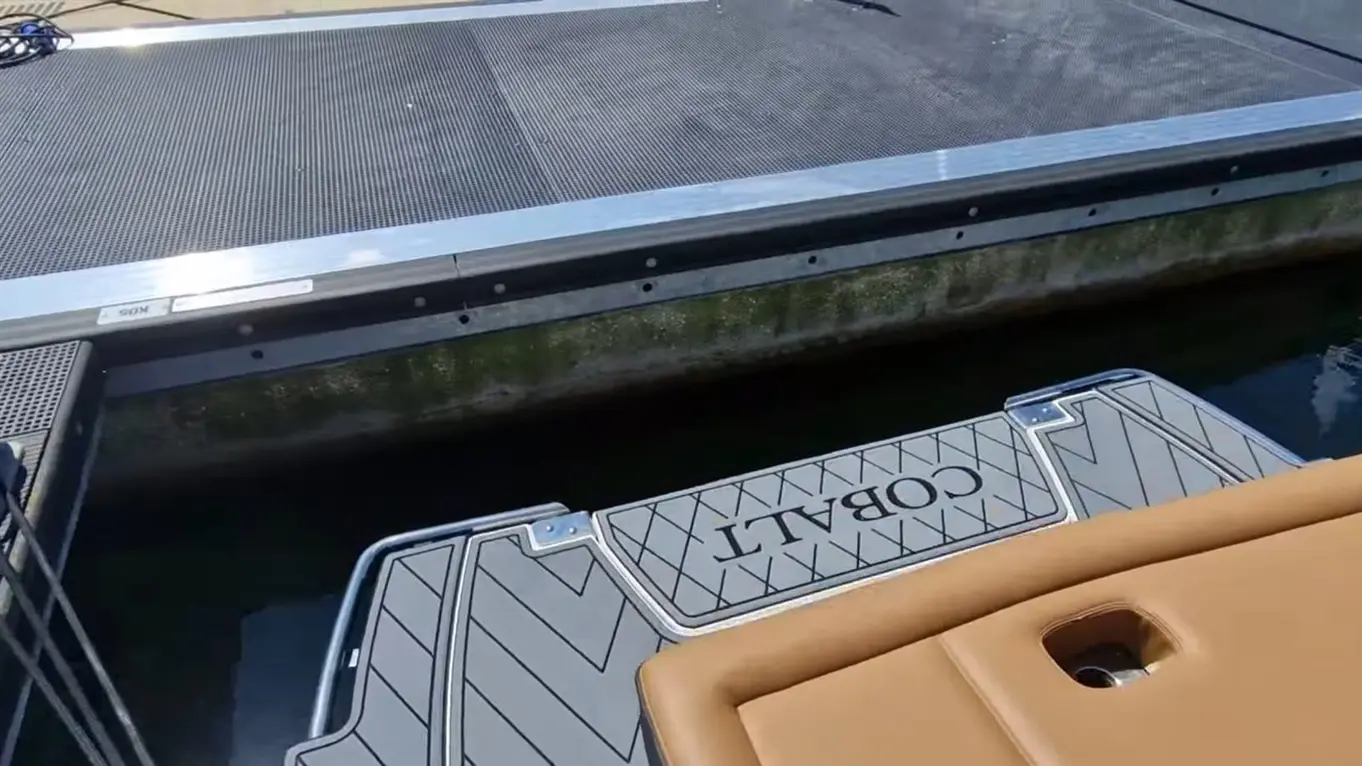 View of a dock with a grey matting, featuring the word "COBALT" on a floating pad, beside tranquil water and a textured surface.
