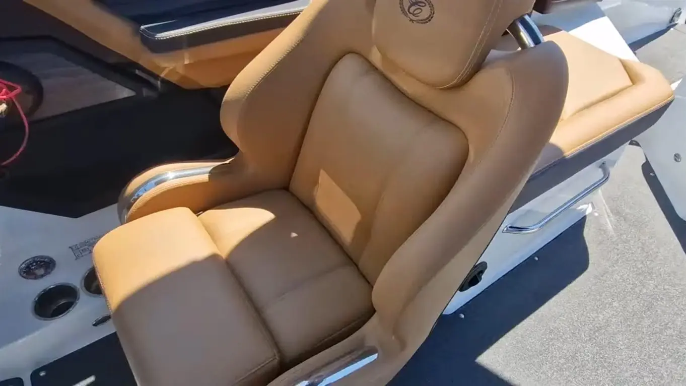 A luxurious tan boat seat with chrome accents, positioned near the steering wheel and control panel on a sunny day.
