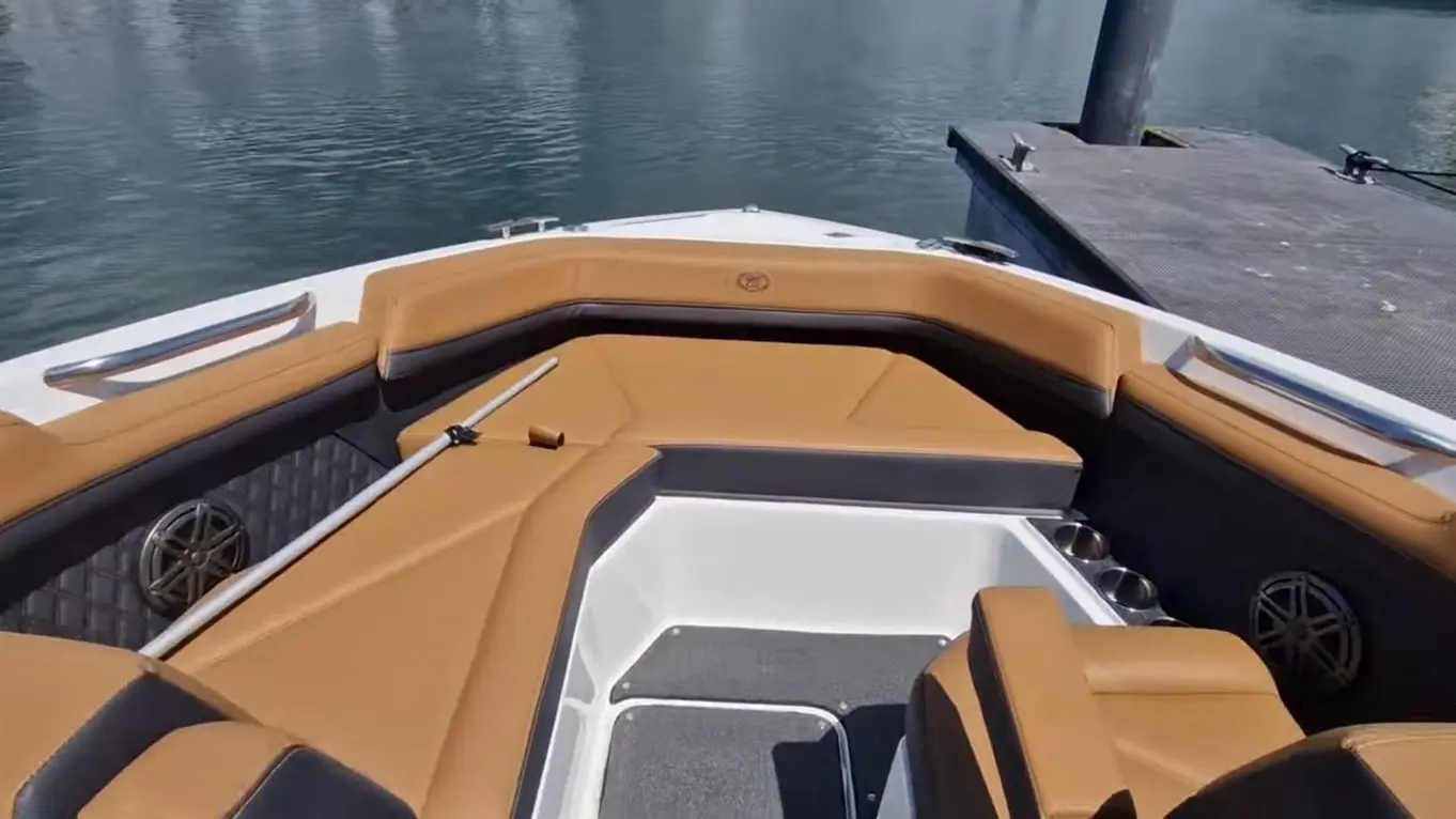 Luxury boat interior featuring tan and grey seating with a view of calm water and a nearby dock.