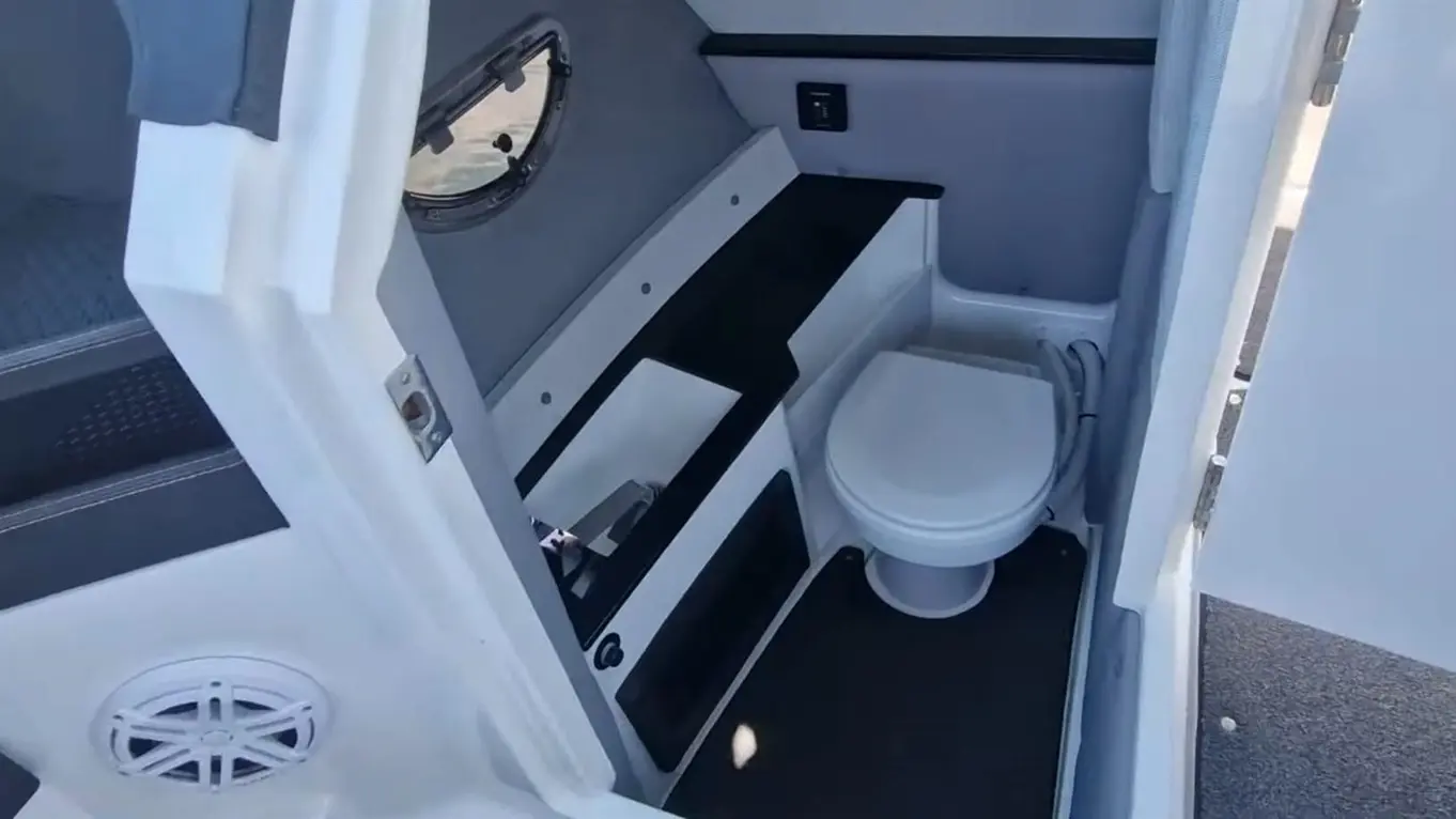 Interior view of a compact boat bathroom featuring a white toilet, dark flooring, and a small countertop with storage.