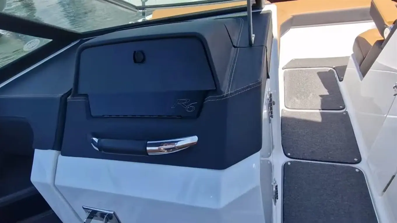 Interior of a boat showing a storage compartment with a chrome handle and R6 logo, alongside textured flooring.