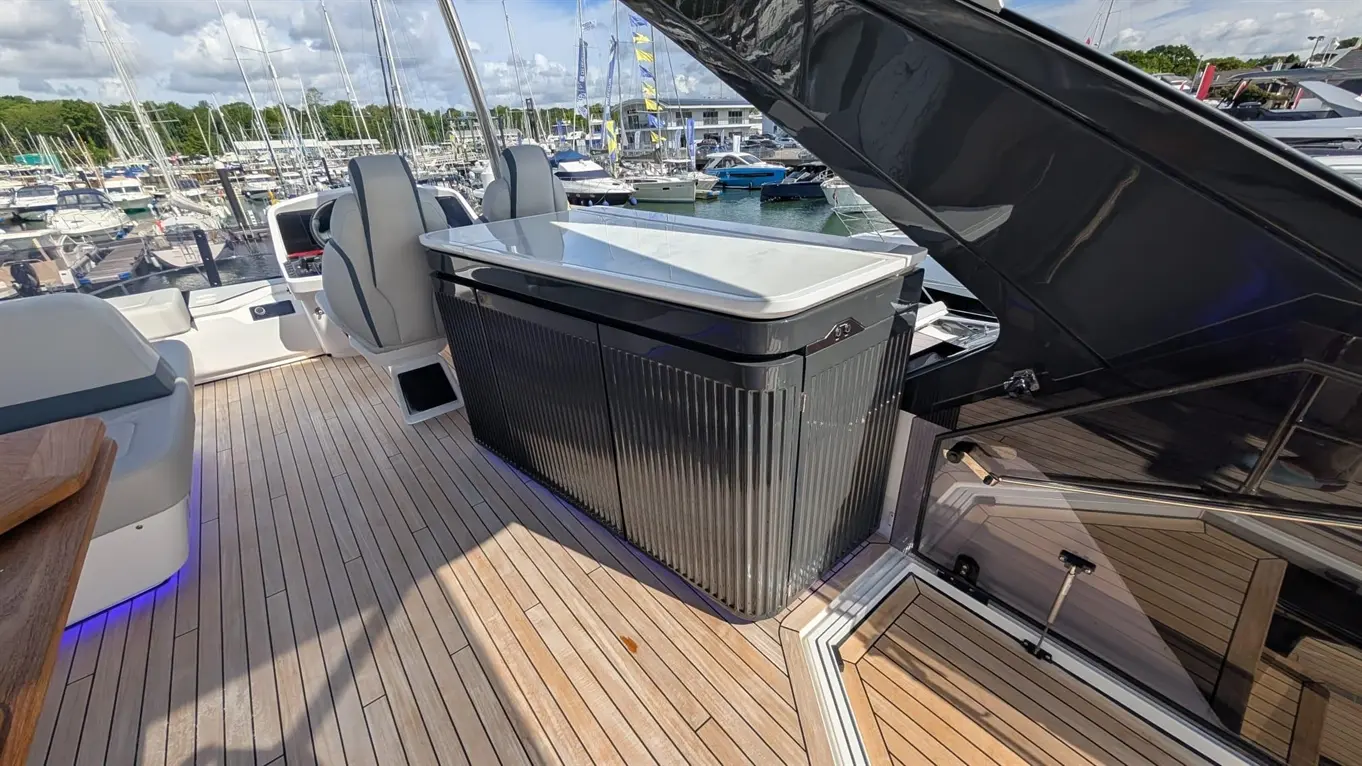 Interior view of a boat with a bar area, seating, and a clear view of a marina filled with boats. Marine environment.