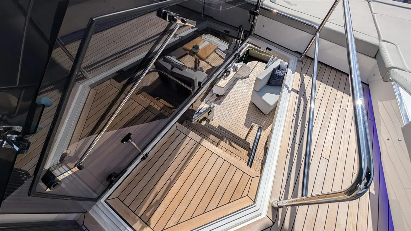 Aerial view of a yacht's deck, featuring wooden flooring, modern seating, and stairway with stainless steel railings.