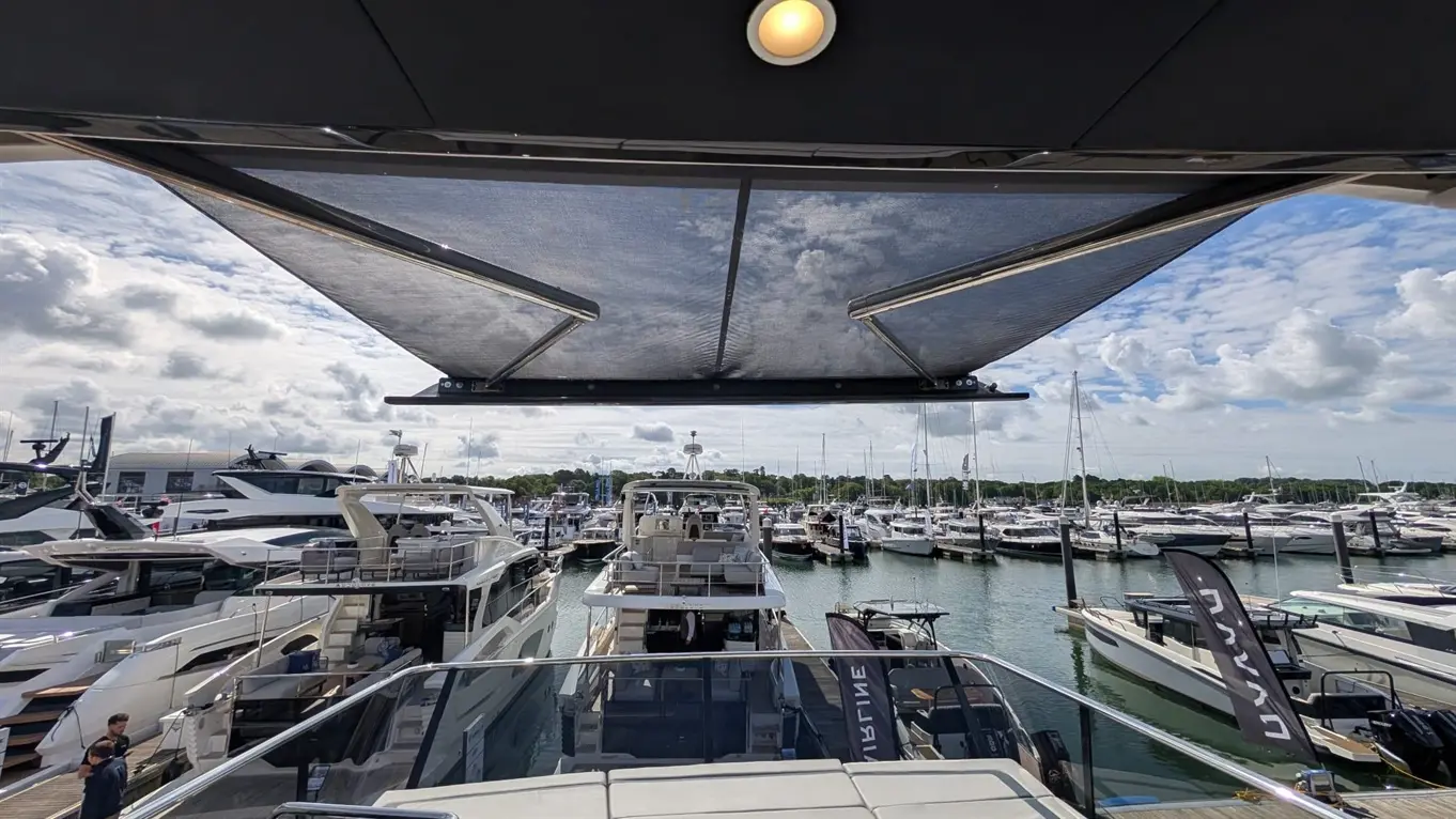 View from a yacht with a retractable sunshade, overlooking a marina filled with various boats and yachts under a cloudy sky.