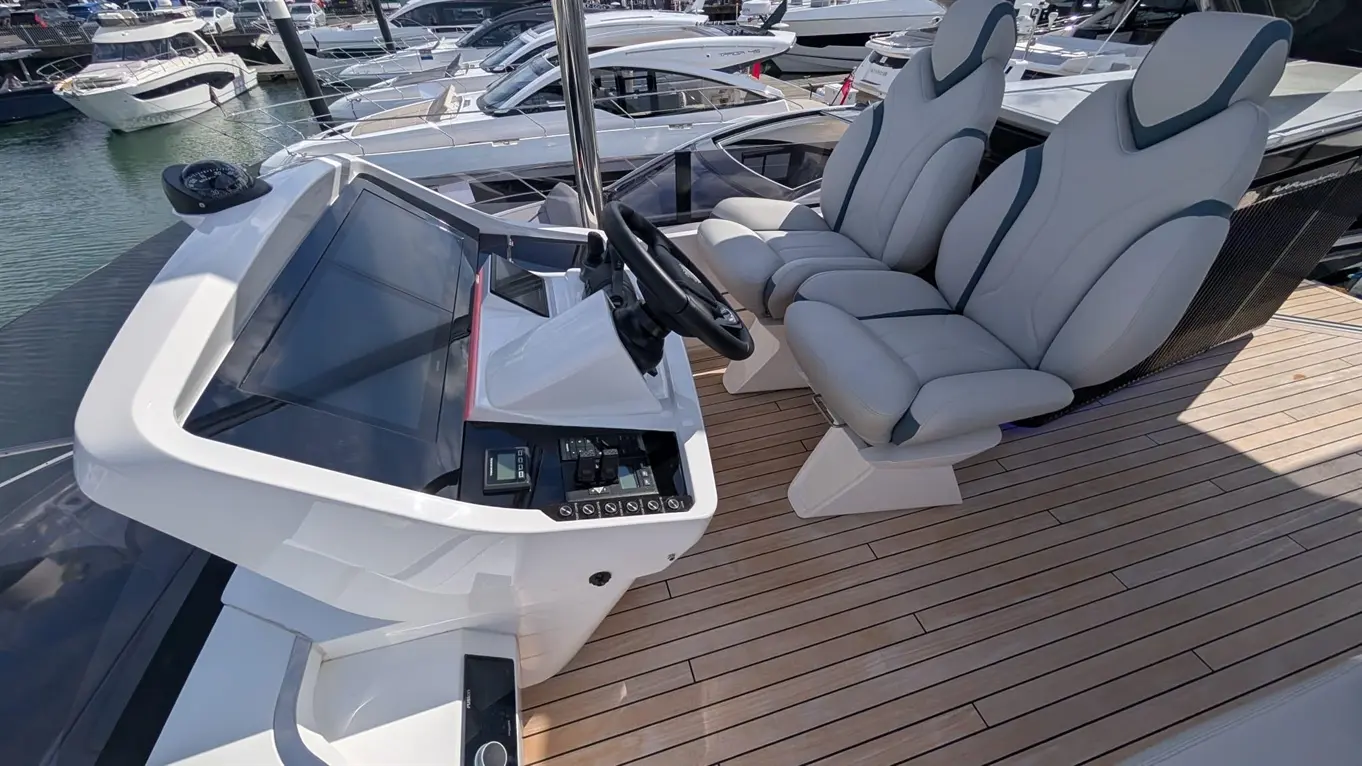 A luxury boat's cockpit featuring a modern steering wheel, two grey ergonomic seats, and sleek dashboard controls on a wooden deck.
