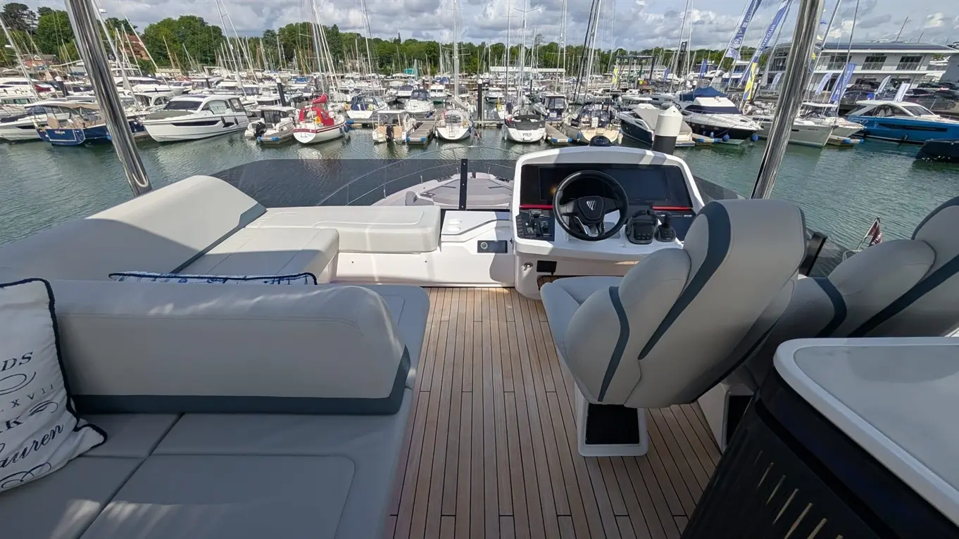 A luxury yacht's helm with a steering wheel and controls, overlooking a marina filled with various boats.