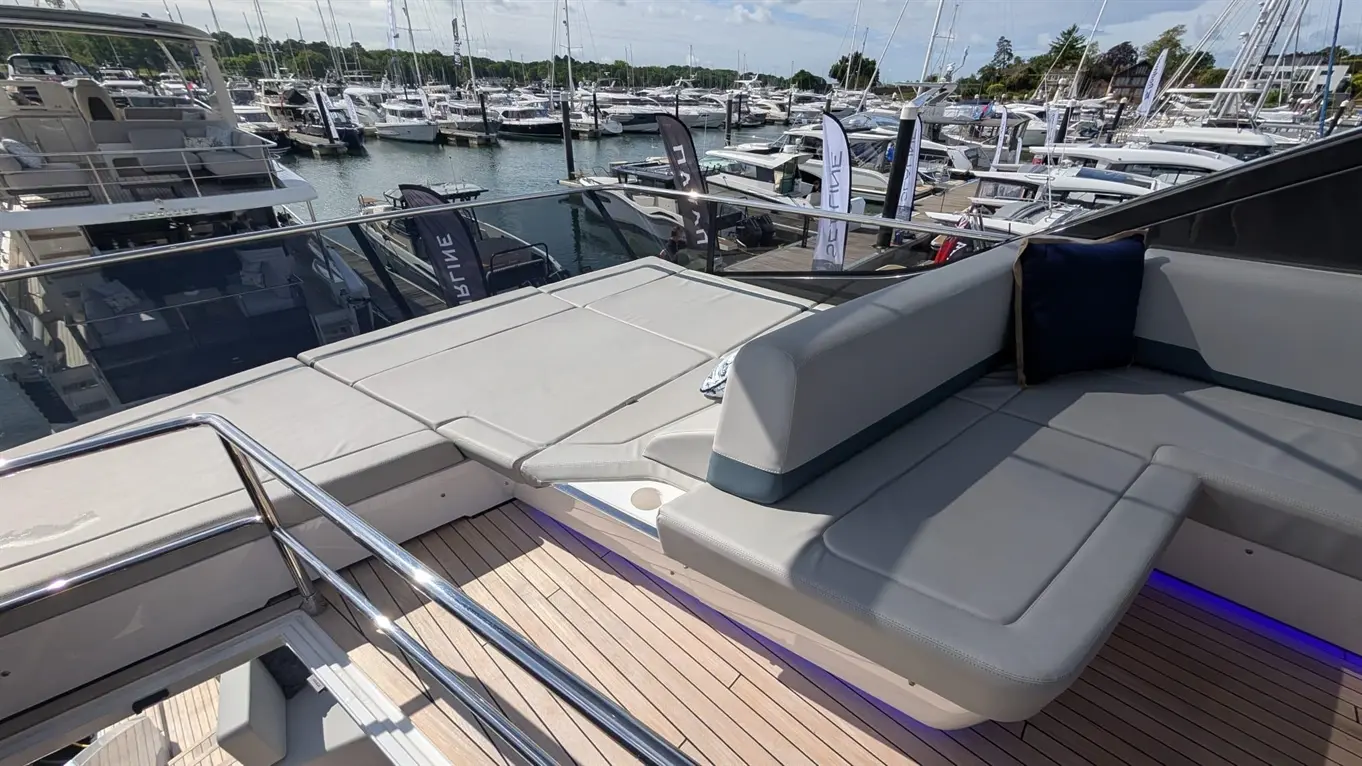 Luxury boat deck with grey seating, overlooking a marina filled with yachts and flags, showcasing a sunny, vibrant day.