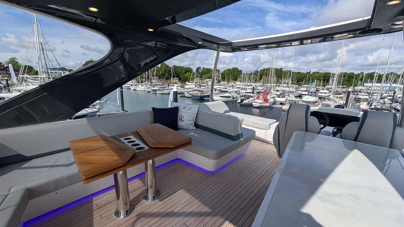Stylish boat interior with modern seating, wooden table, and marina view featuring multiple yachts and sailboats.