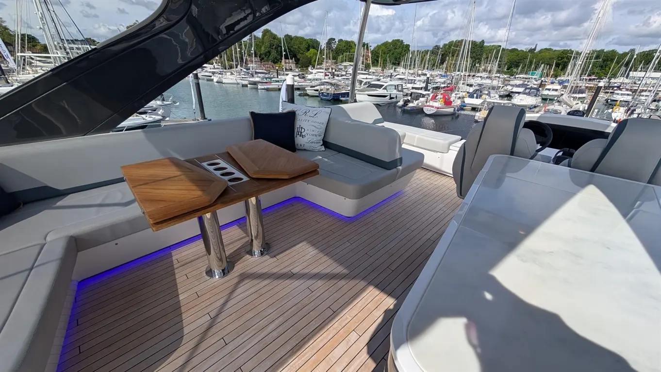 Luxury boat deck featuring seating, a wooden table, and blue LED lighting, overlooking a marina filled with boats.