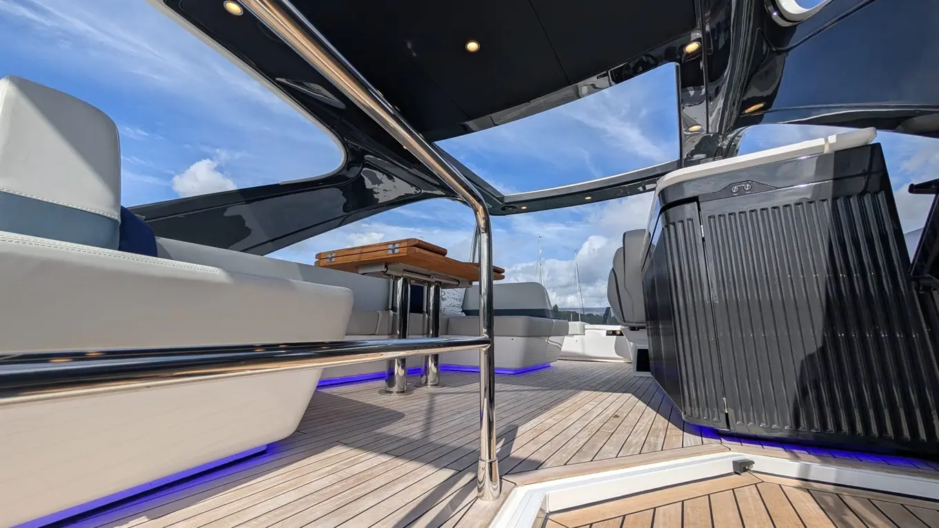 Interior of a modern boat featuring sleek seating, a wooden table, and ambient blue lighting under the deck.