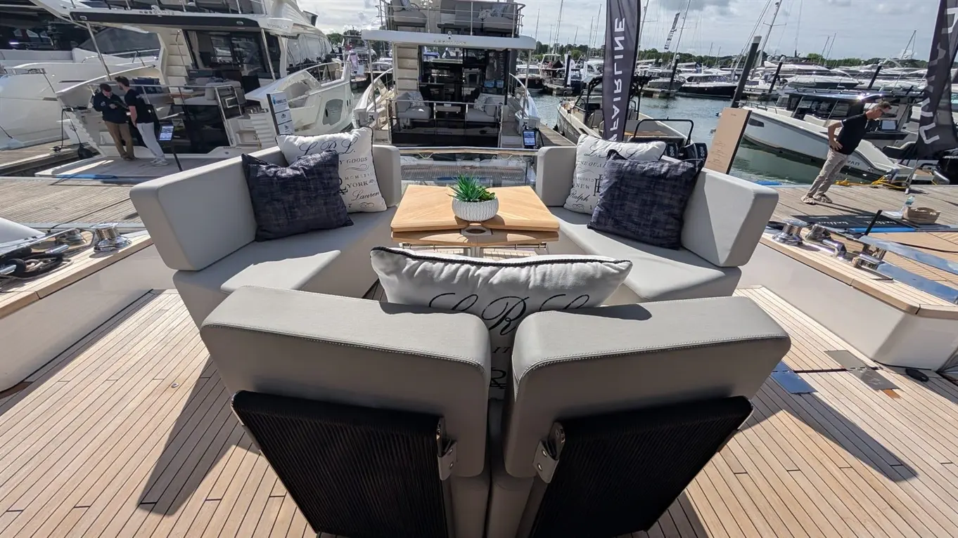 Stylish outdoor seating on a yacht deck, featuring cushions, a wooden table, and a small plant, with boats in the background.