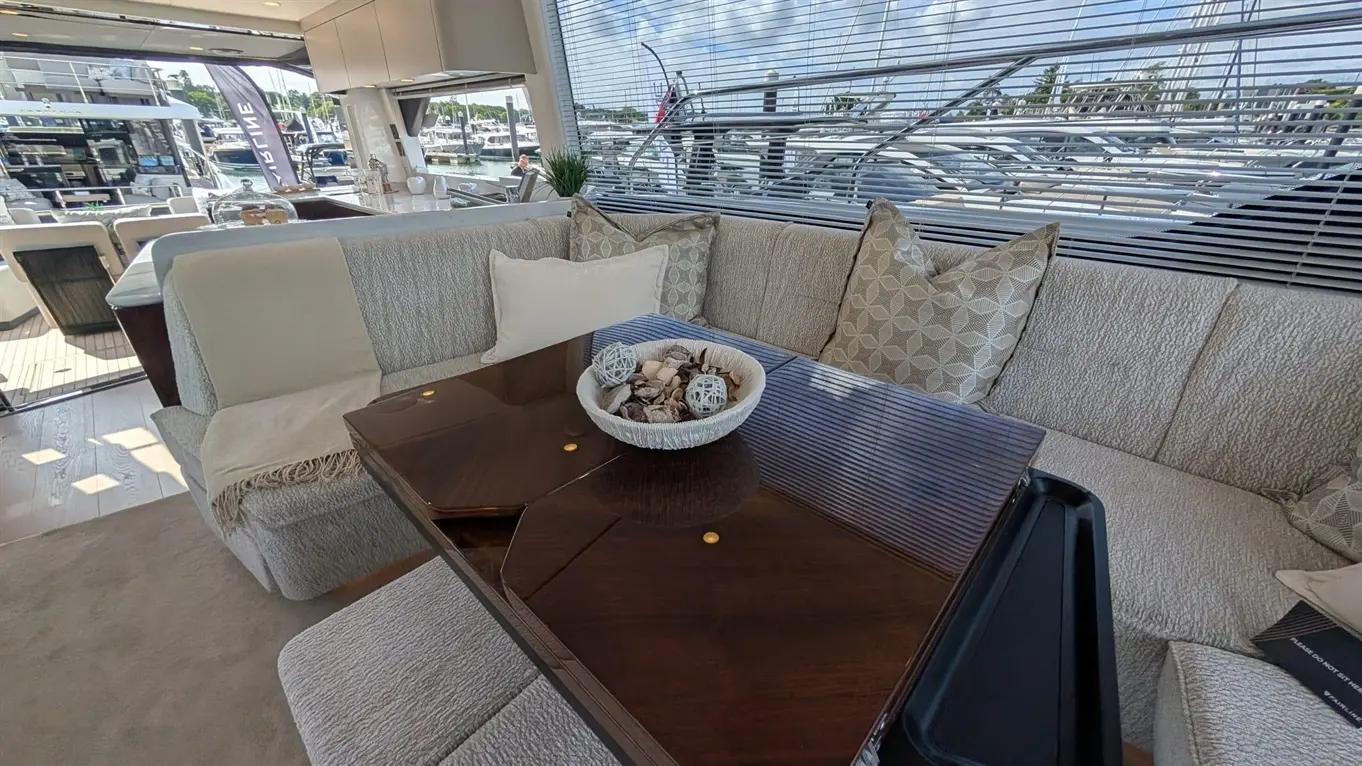 Modern boat interior with a textured sofa, a glossy table, and a decorative bowl of shells, overlooking a marina.