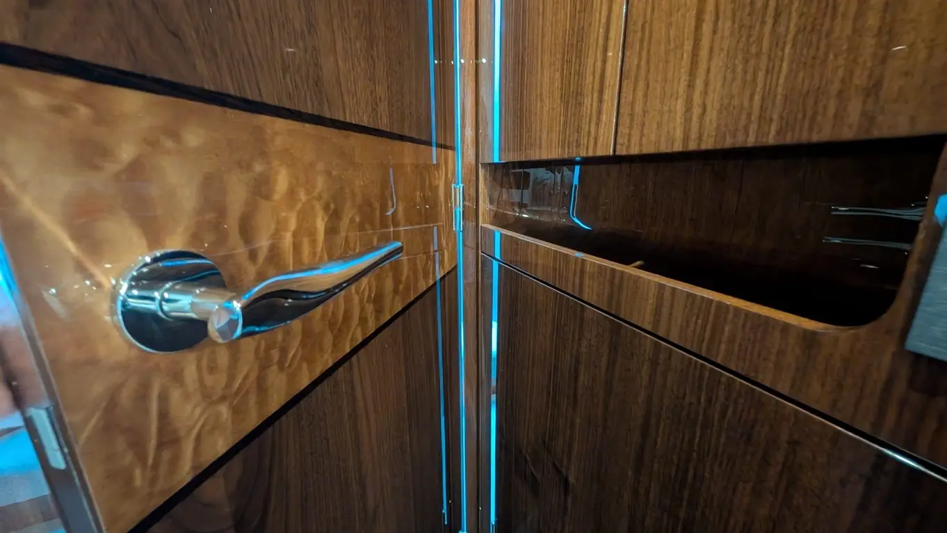 A close-up of a sleek wooden cabinet with a silver handle, featuring blue LED lighting along the edges.