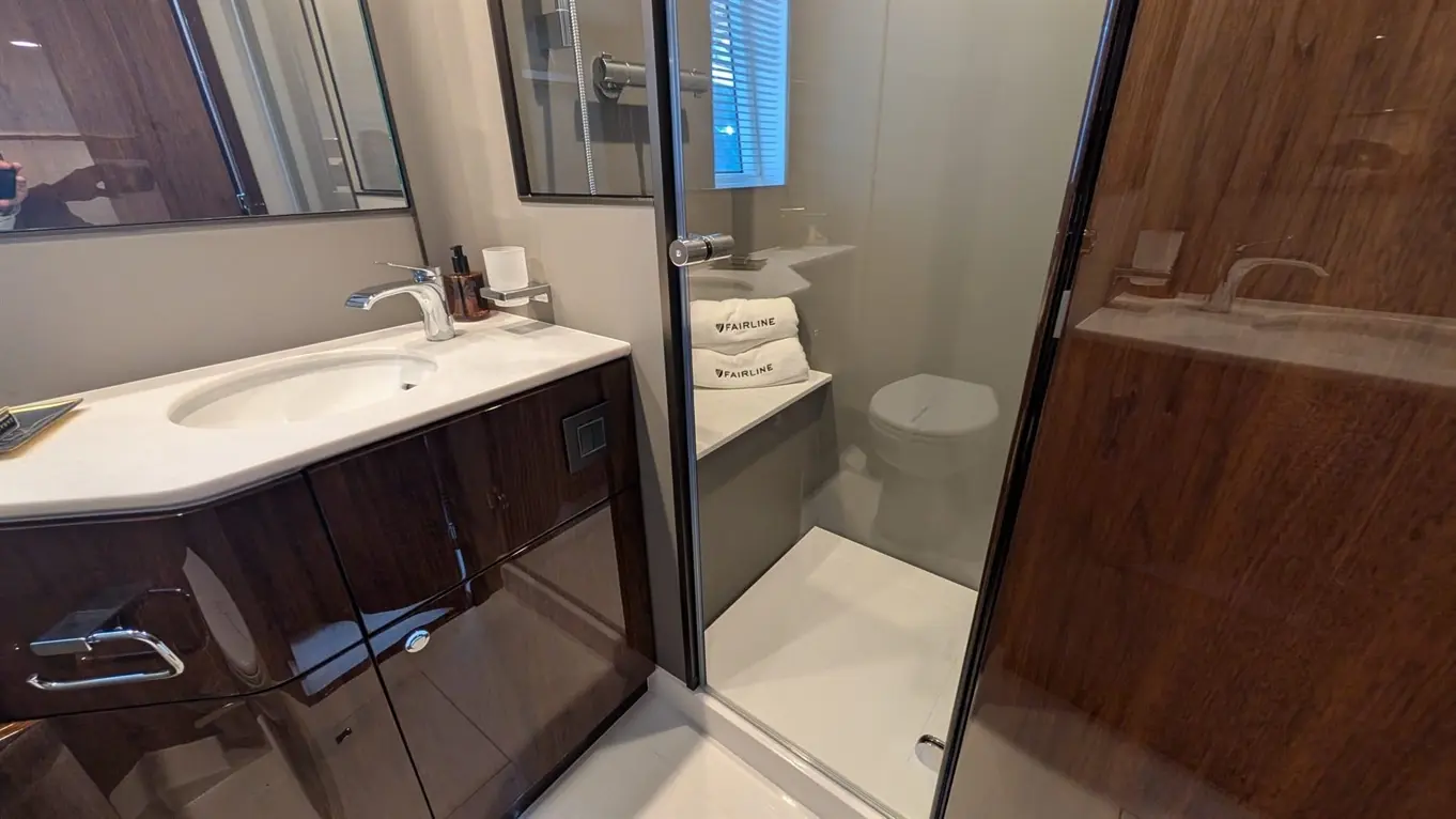 Modern bathroom featuring a glass shower, sink with a chrome faucet, wooden cabinets, and neatly stacked Fairline towels.