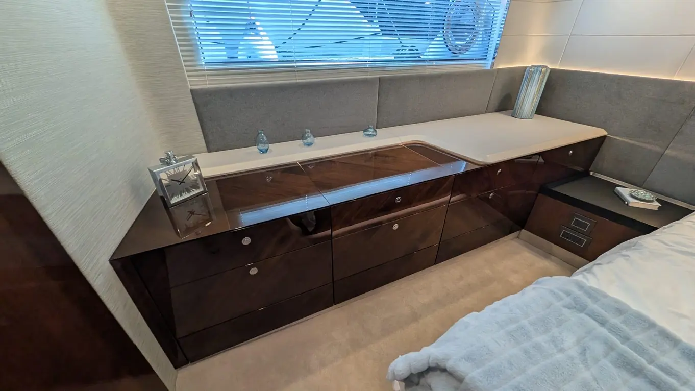 Modern bedroom interior featuring sleek wooden storage unit, clock, glass decorations, and soft furnishings by a window.