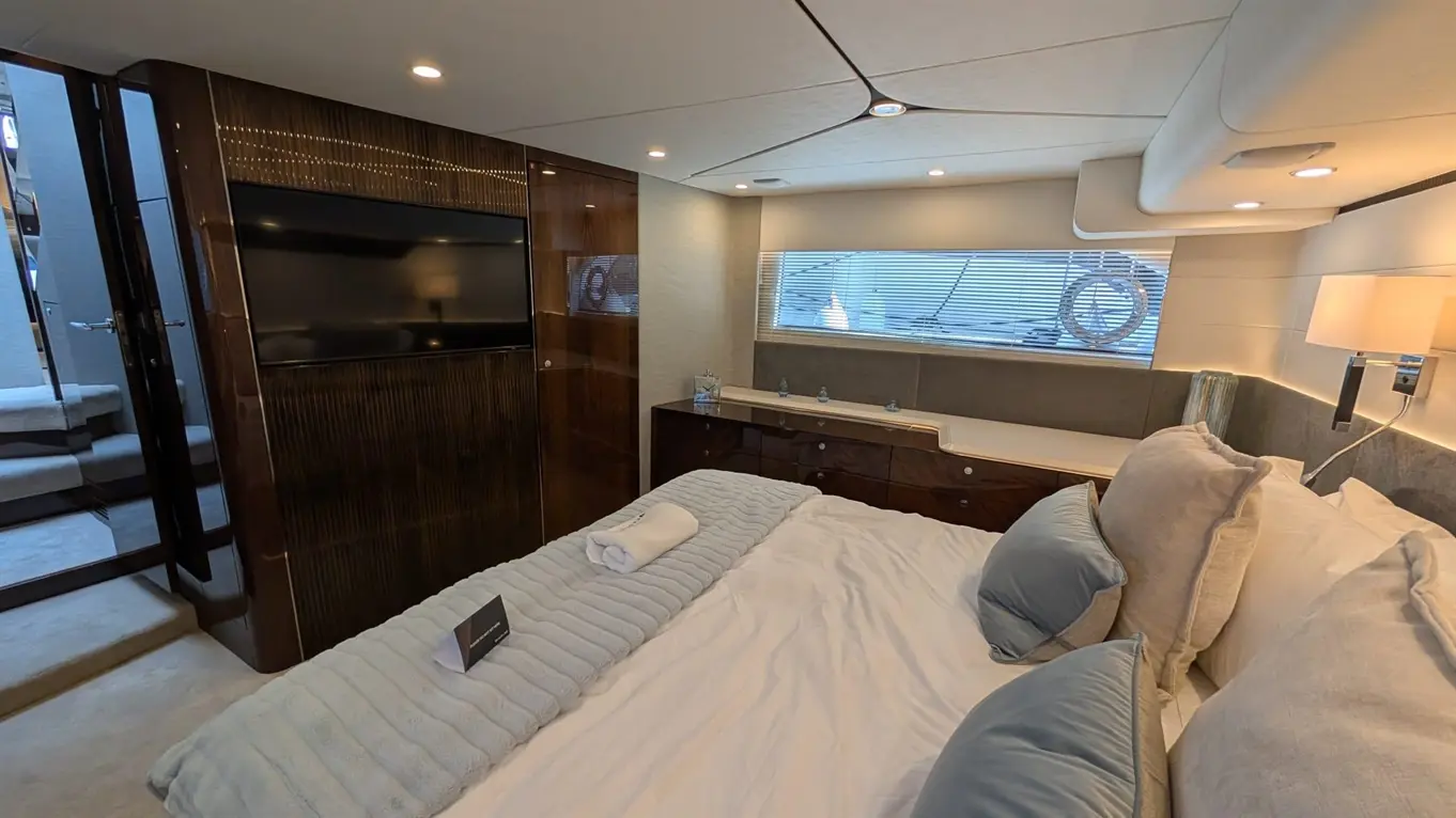 Luxurious boat bedroom with a large bed, TV, stylish decor, and a window overlooking the water, featuring soft furnishings.