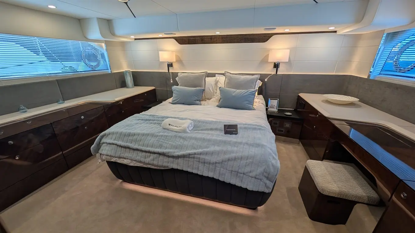 Modern yacht cabin featuring a king-size bed, soft furnishings, ambient lighting, and stylish wooden furniture.