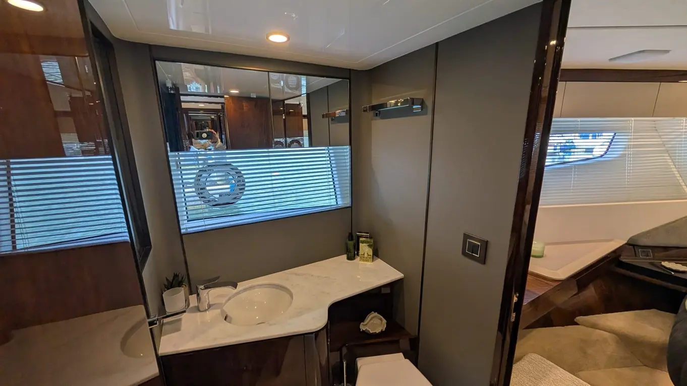 A sleek yacht bathroom featuring a marble sink, stylish mirror, and natural light from blinds, with green toiletries on display.