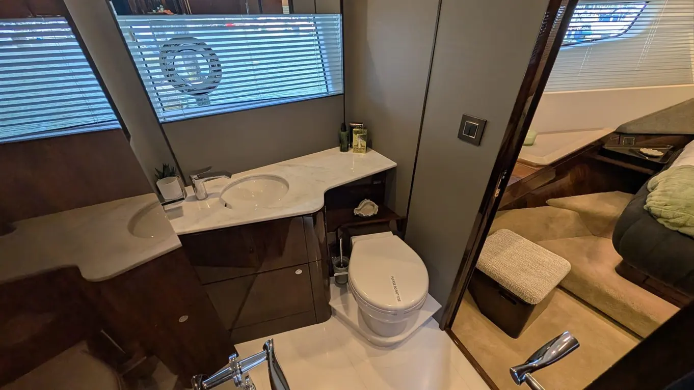 Modern boat bathroom featuring a white sink, toilet, and marble countertop beside a window with horizontal blinds.