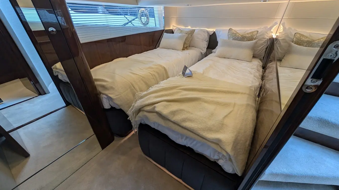 Interior of a luxury cabin featuring two single beds, decorative pillows, a plush throw, and modern glass elements.