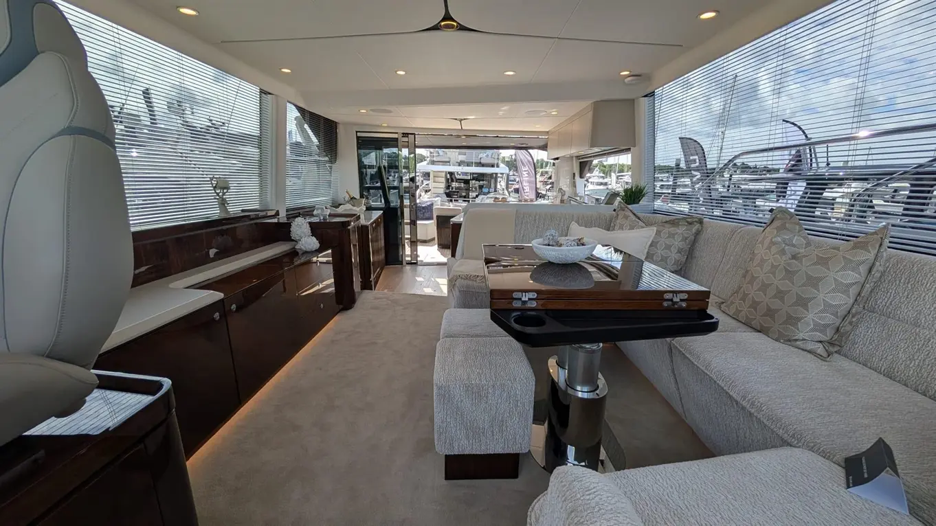 Luxurious yacht interior featuring plush seating, a glass dining table, elegant decor, and views of boats through large windows.