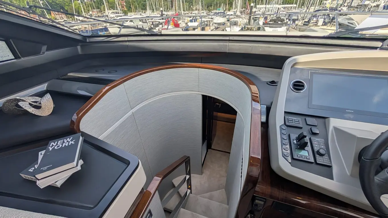 Interior of a yacht showing stairs leading below deck, a navigation console, and a decorative metal sculpture with books.