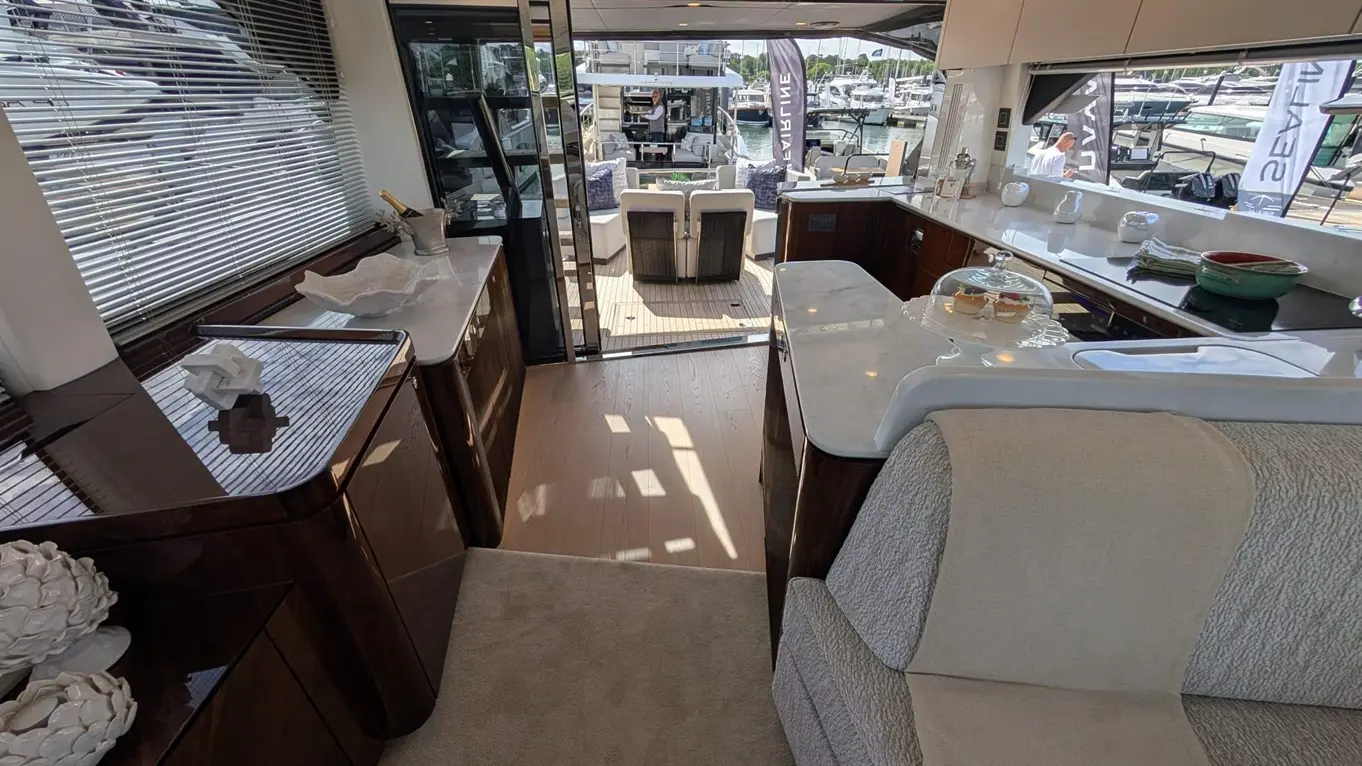Interior view of a yacht, featuring a modern kitchen with a seating area and large windows overlooking the marina.