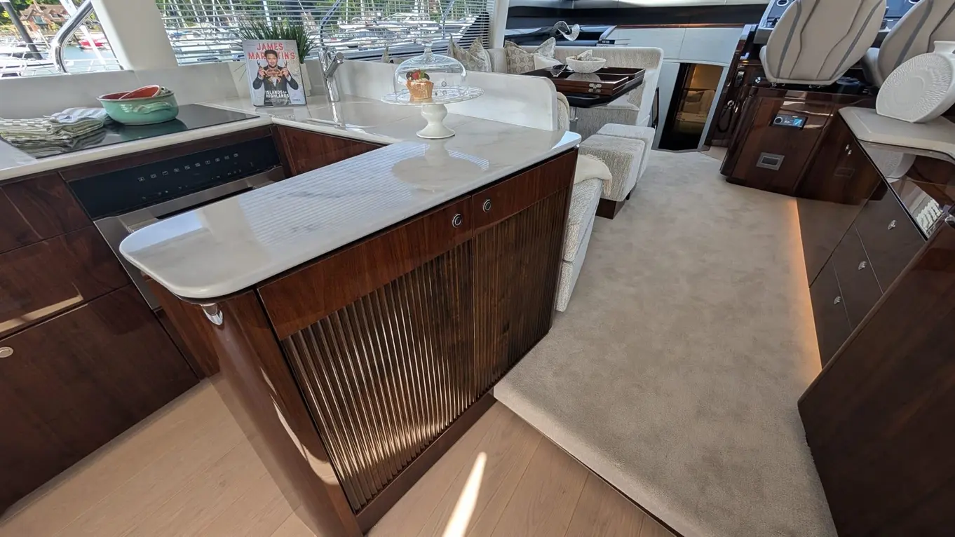 Luxury yacht interior featuring a modern kitchen with a marble countertop, wooden cabinets, and a cupcake display.