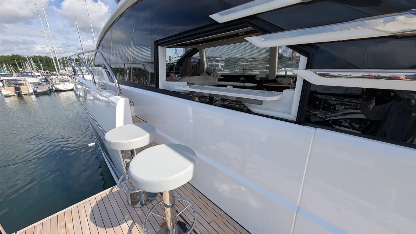 Luxury yacht exterior with stylish bar stools, overlooking a marina filled with boats, featuring large glass windows.