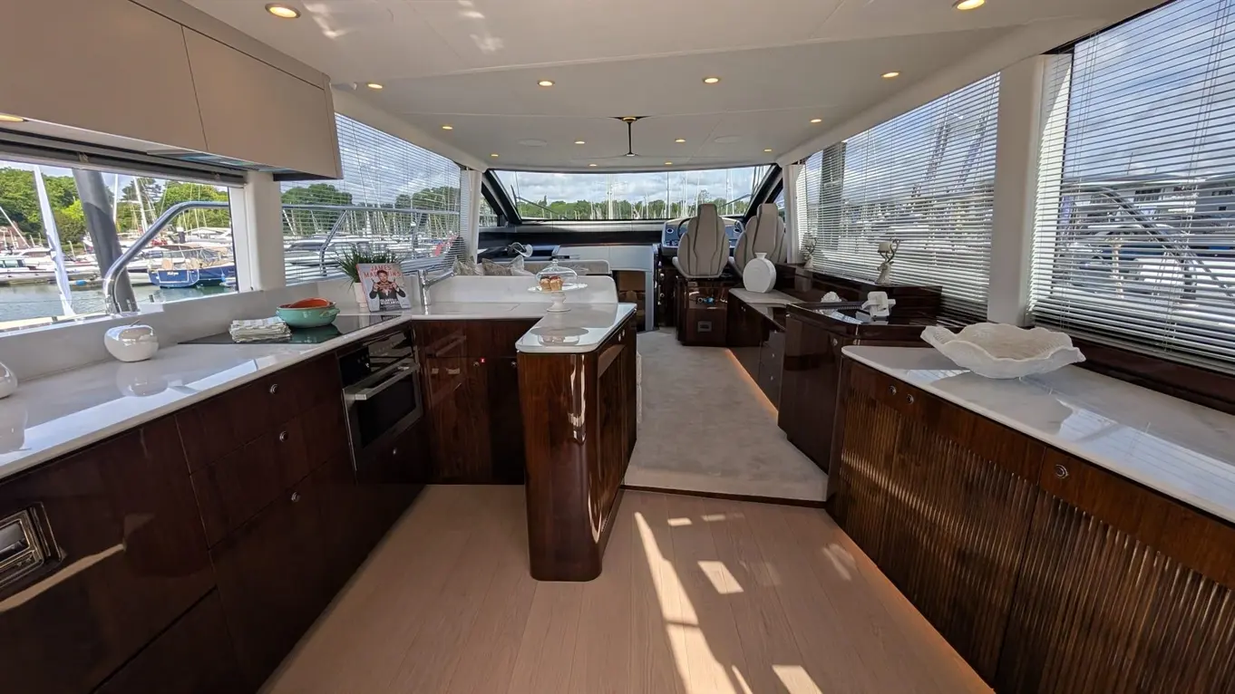 Luxury yacht interior featuring a modern kitchen, seating area, and views of boats in the marina through large windows.