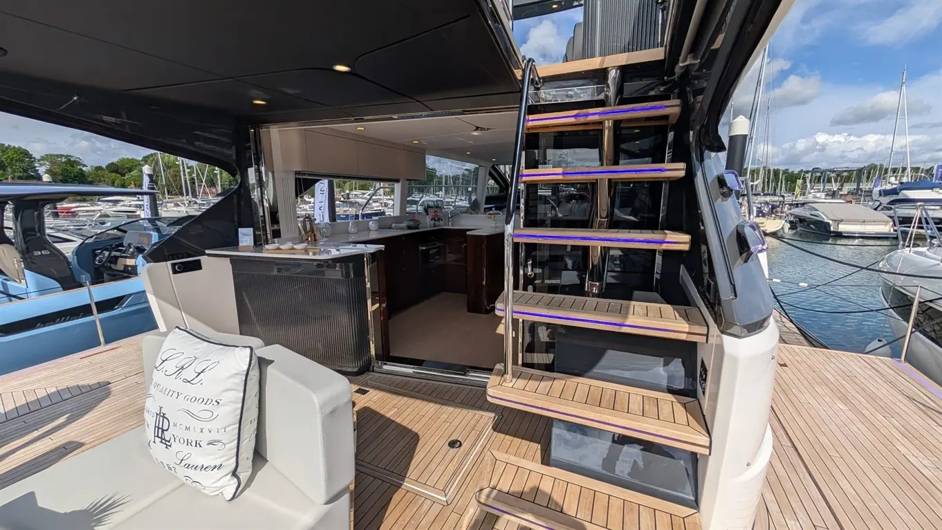 Luxurious interior of a boat showing a kitchen area, a white outdoor cushion with text, and stylised stairs leading above.