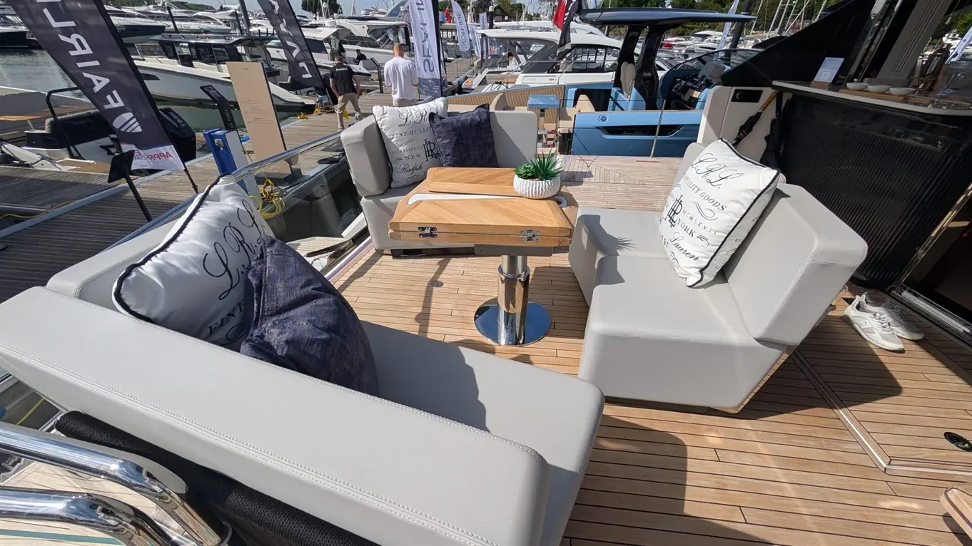 Luxury boat seating area with modern grey sofas, a wooden table, and decorative cushions overlooking a marina.
