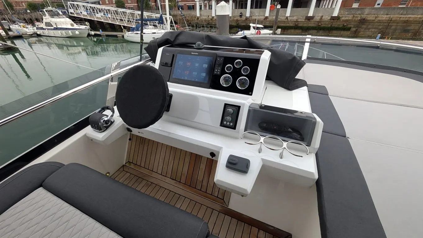 Modern boat helm featuring a touchscreen display, gauges, and a pair of glasses on a sunbed, overlooking a marina.