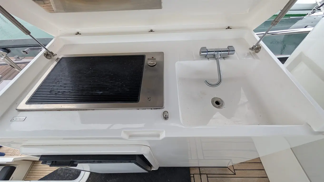 Marine outdoor kitchen featuring a grill and sink, with a stainless steel faucet and draining hole visible.