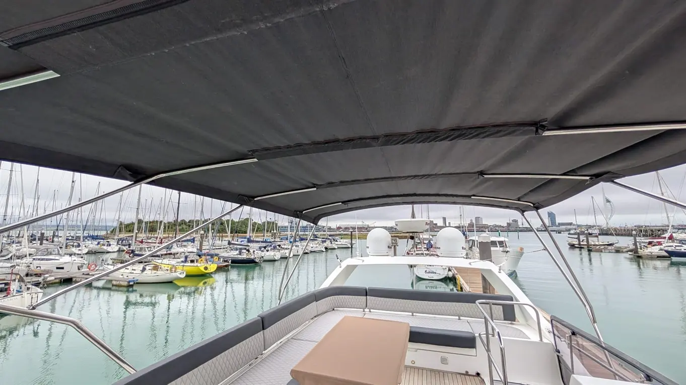 View from a yacht showcasing a marina filled with boats, under a large black canopy with a table in the foreground.
