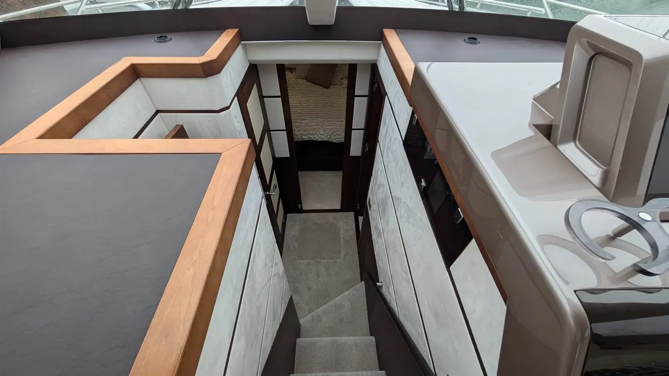 Modern yacht interior view showing stylish steps leading to a cabin with cream bedding and sleek wooden accents.