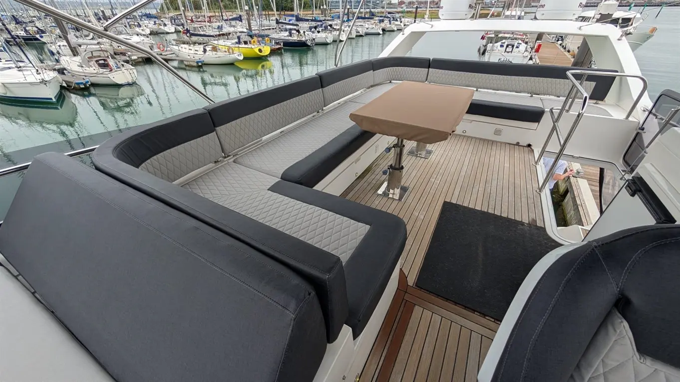 Luxurious yacht deck featuring grey seating, a central table, and views of moored boats in the marina.
