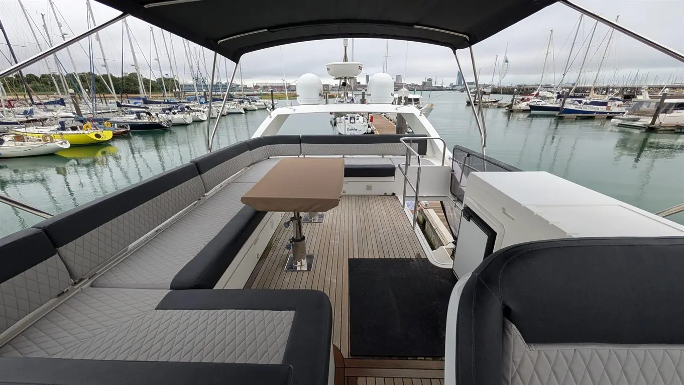 Luxury yacht deck with seating and table, overlooking a marina filled with sailboats and yachts under a cloudy sky.