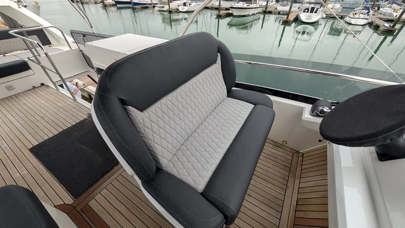 Comfortable grey and black seating on a yacht deck, overlooking boats in the marina, with polished wooden flooring.