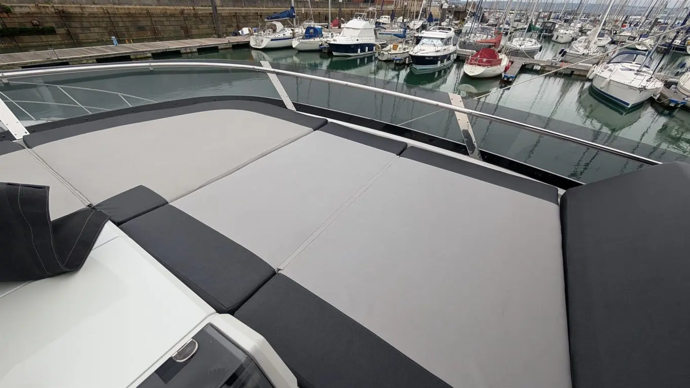 Luxury yacht deck with grey and black cushions overlooking a marina filled with boats and calm waters.