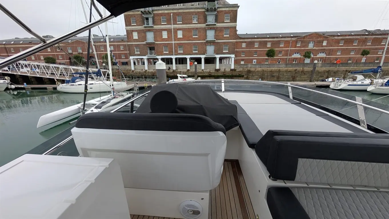 View from a boat towards a marina with several yachts and a brick building in the background, set on calm waters.