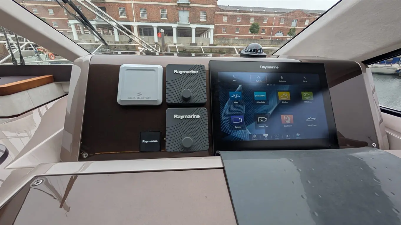 Boat control panel with a Raymarine touchscreen, Seakeeper unit, and various switches in a marina setting.