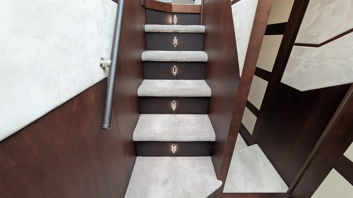 Staircase with grey carpet steps, wood finish, and subtle lighting along the side, leading to an upper level.