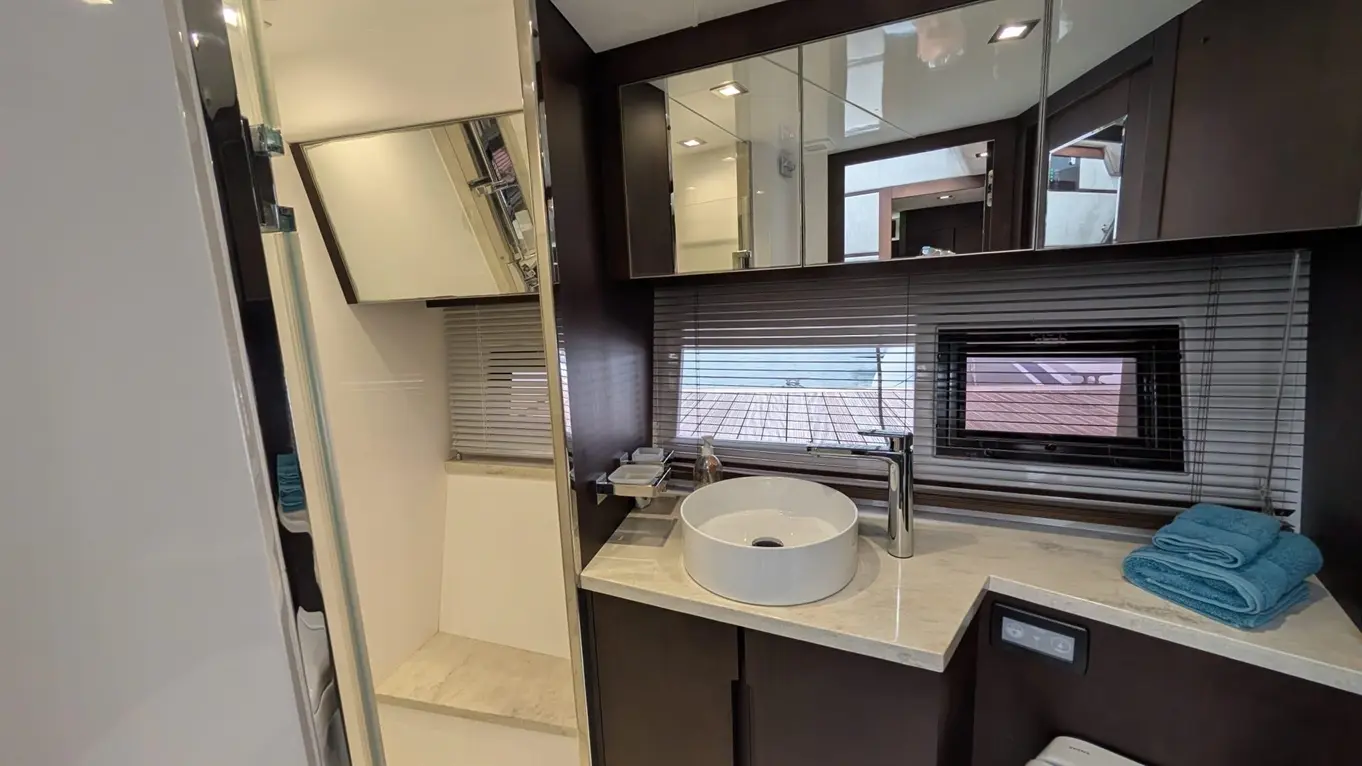 Modern boat bathroom featuring a round sink, marble countertop, mirrored cabinet, and window with blinds.