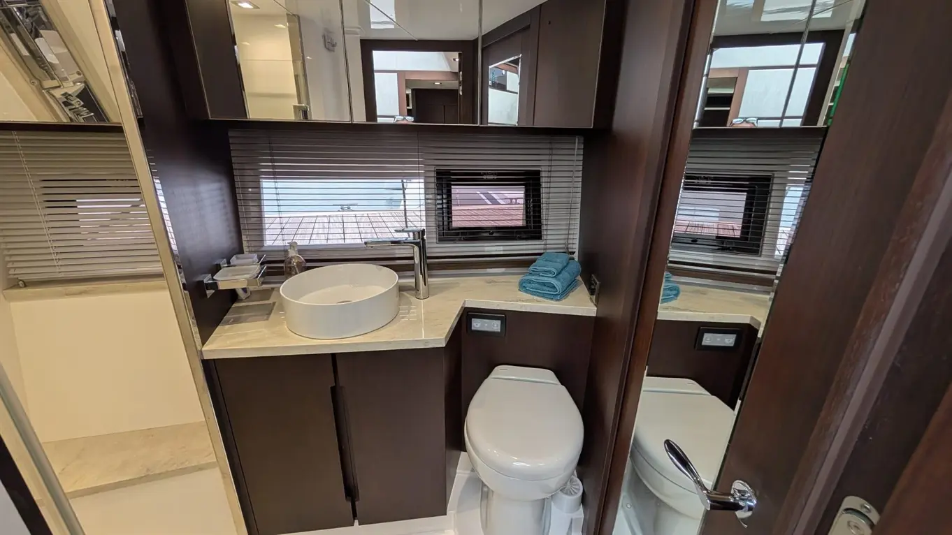 Modern bathroom featuring a round basin, towel storage, and a toilet, with mirrored cabinets and natural light through blinds.