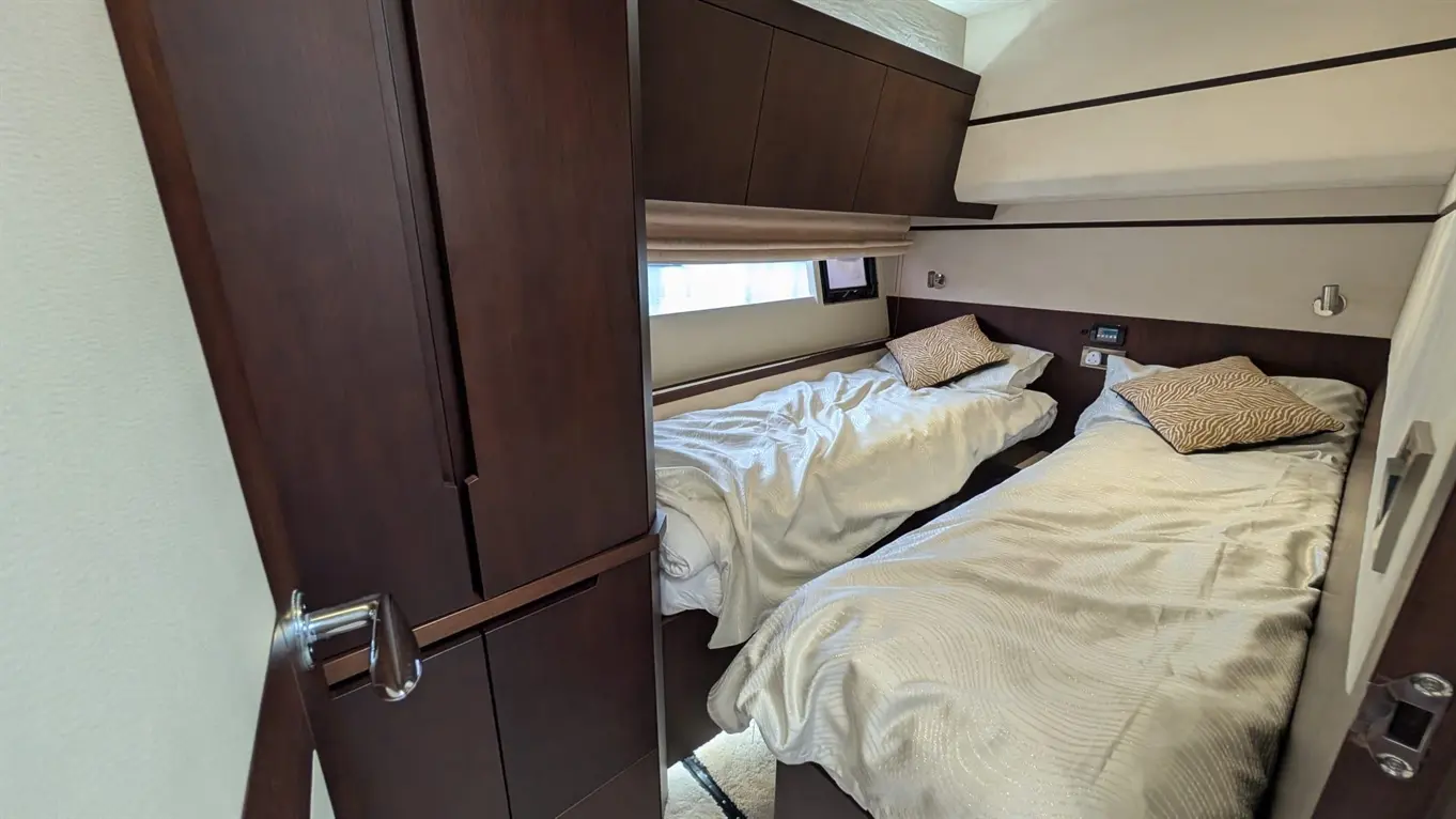 A compact bedroom featuring two single beds with textured white bedding and decorative cushions, alongside a wardrobe and window.